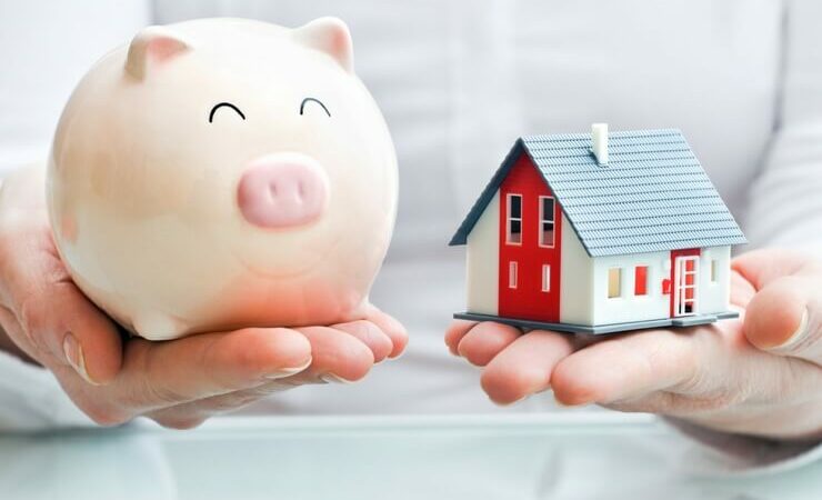 Person holding piggy bank and miniature house FI