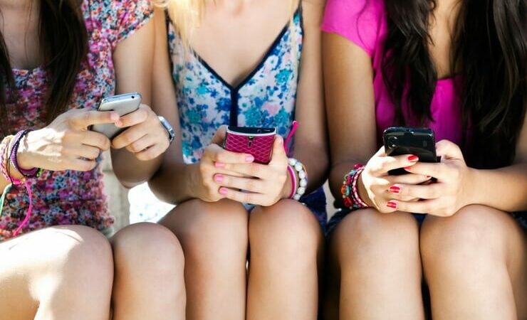 3 girls sitting down and holding cell phones FI