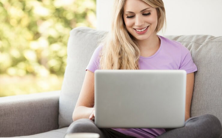 Woman in light pastel t-shirt smiling and typing on laptop computer FI