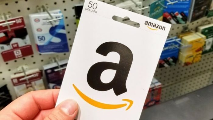 Hand holding $50 Amazon gift card in front of gift card display FI