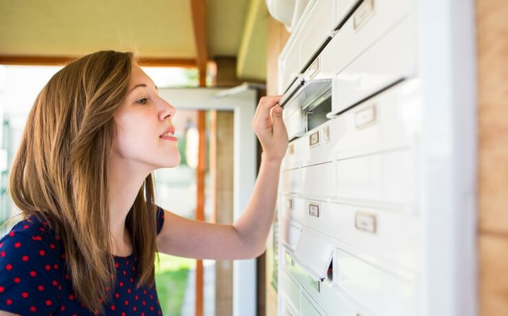 Woman in polka dot dress checking apartment mailbox FI
