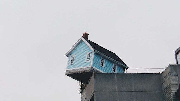 Small blue house sitting on edge of building looking like it might fall