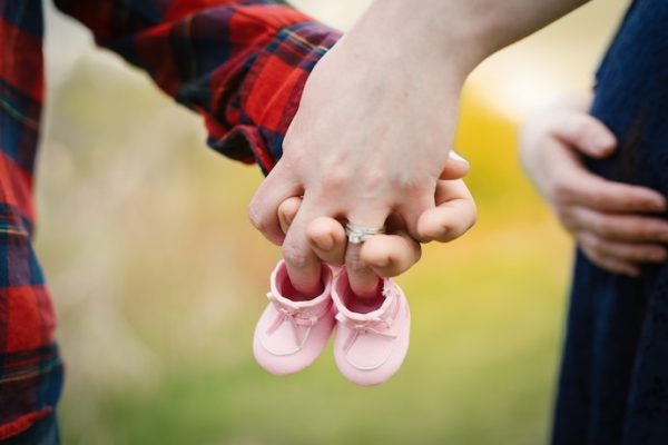 Couple holding hands and pink baby shoes