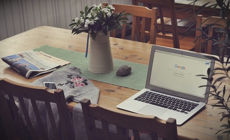 laptop sitting on a table next to sweater and pitcher of flowers