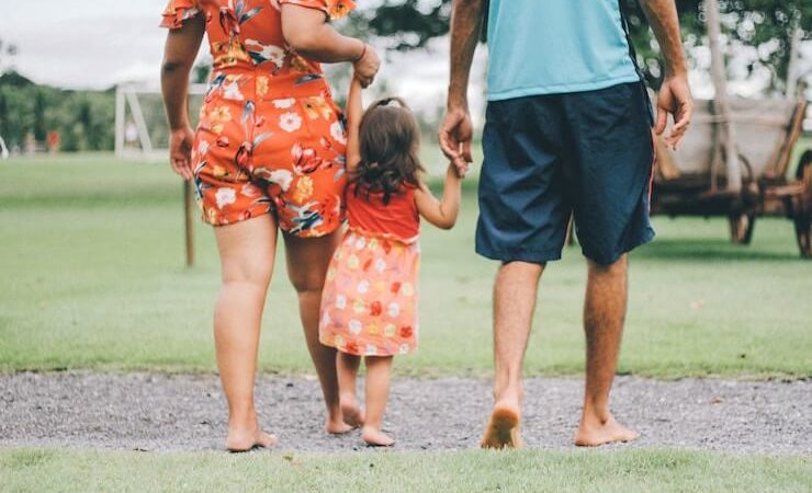 Family of 3 holding hands and walking on grass outside barefoot