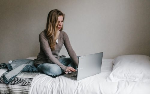 Donna che per mezzo del suo computer portatile acer sul suo letto accanto alla sua giacca di jeans