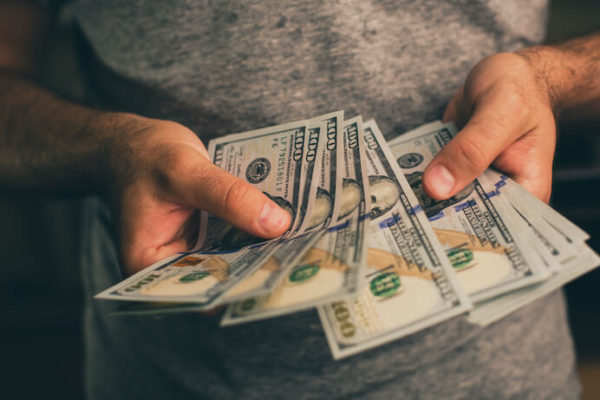 Man holding hundreds of dollars wearing a grey shirt