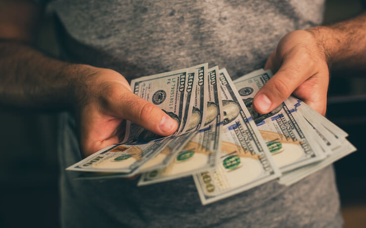 Man holding hundreds of dollars wearing a grey shirt