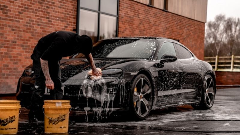 photo of a person washing a black car with yellow buckets in mobile car wash service
