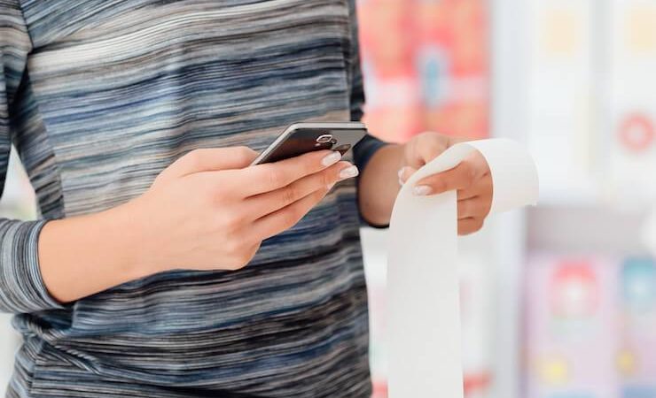 Woman wearing black and blue striped shirt holding a receipt and cell phone