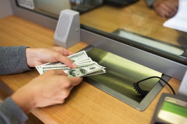 Woman withdrawing hundreds of dollars from bank teller at a bank