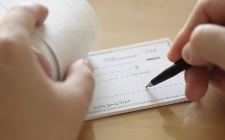 Person writing a check on beige table