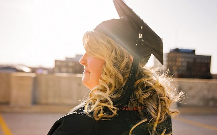 Graduate looking to the horizon while smiling with big blonde curls