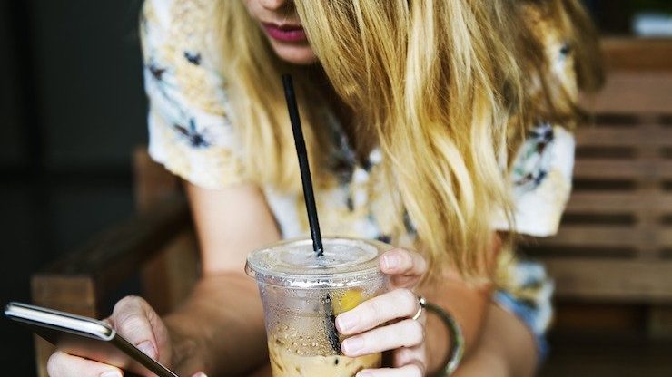 Woman looking at her phone while holding her iced coffee