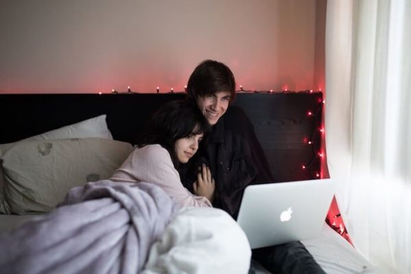 young couple watching a movie on their apple laptop while cuddling in bed