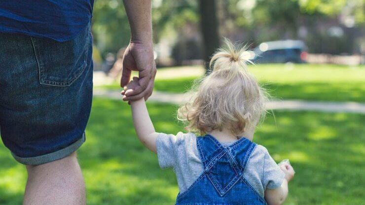 Little girl in blue jean overalls holding her fathers hand who is wearing blue jean shorts