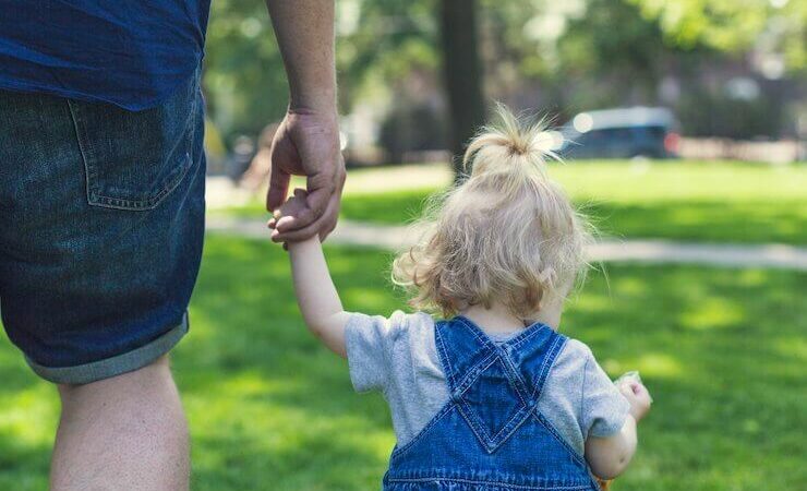 Little girl in blue jean overalls holding her fathers hand who is wearing blue jean shorts
