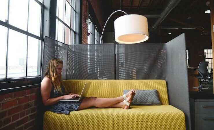 Blond girl using her computer on a yellow couch