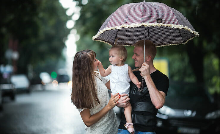 A happy family outside holding umbrella to protect from rain and sun