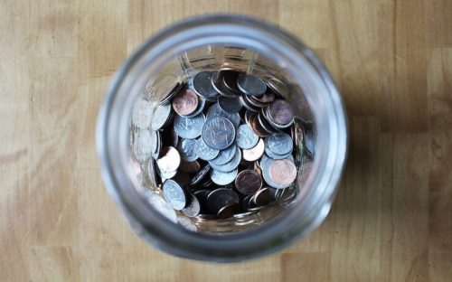 Große Glasvase voller Münzen auf einem Holztisch