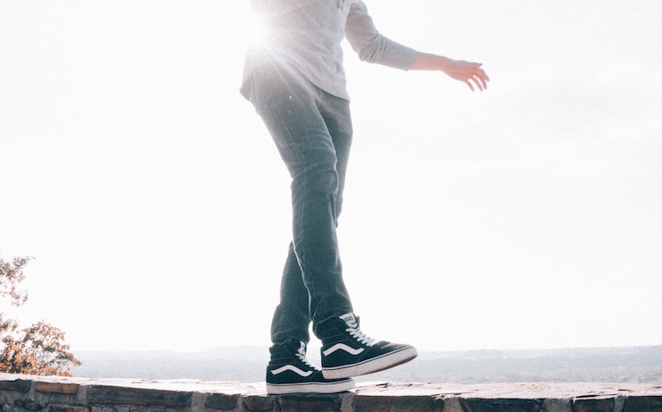 Man balancing on a wall wearing black sneakers and jeans