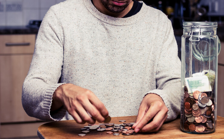 Man counting out coins on a table from a jar