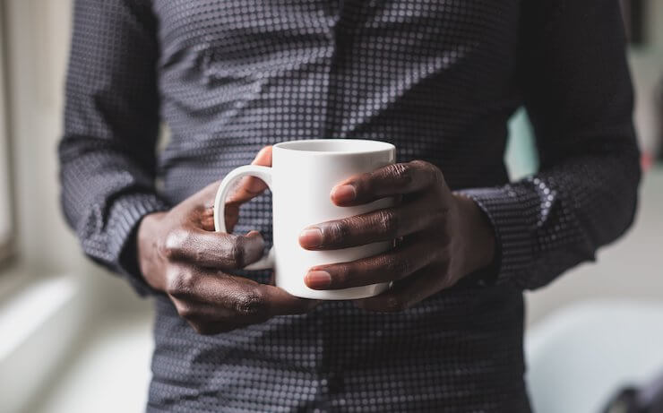 Man in a dotted grey shirt holding a white mug with coffee