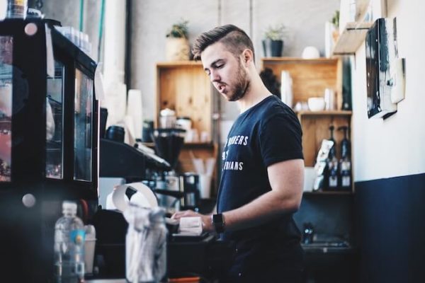 Young man working minimum wage job at coffee shop to make ends meet