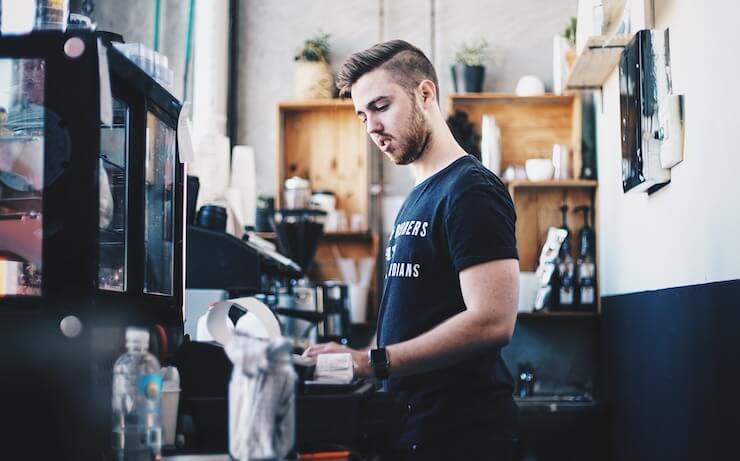 Young man working minimum wage job at coffee shop to make ends meet