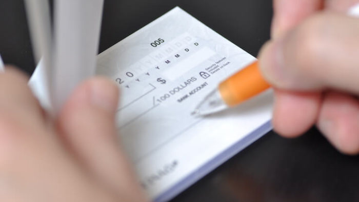 Person filling out a check in their checkbook using a pen with orange grip