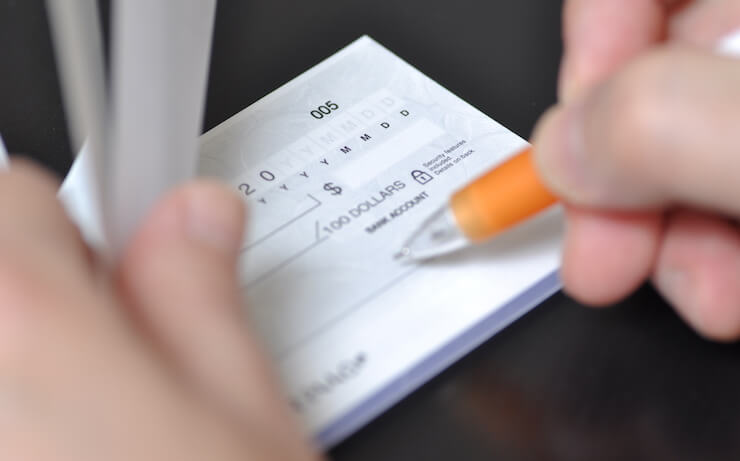 person filling out check in checkbook with orange pen