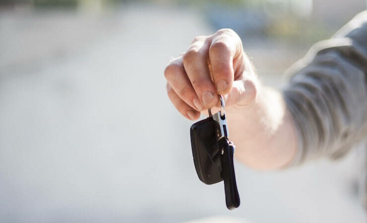 Person handing car keys to their new owner blurred background