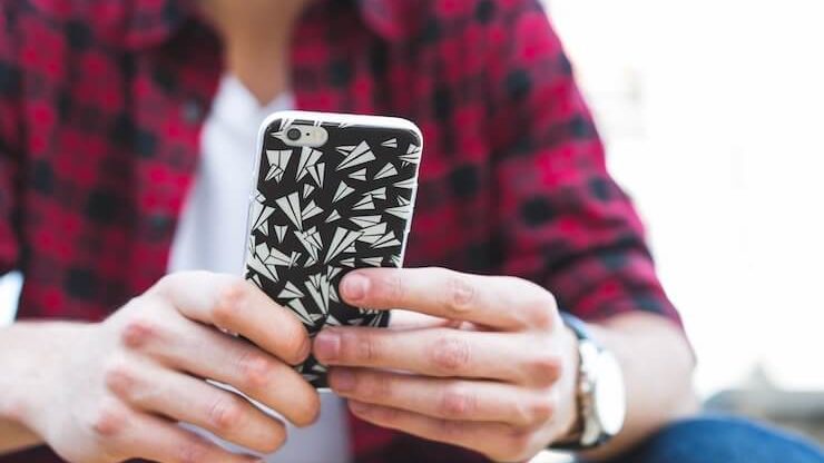Person wearing a red plaid shirt holding a phone with black and white case with paper airplane shapes