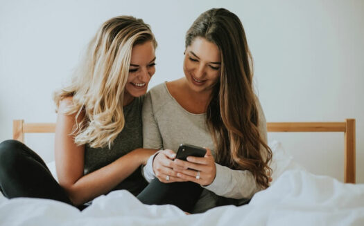 Two women looking at a phone looking at grabpoints while chilling on a bed