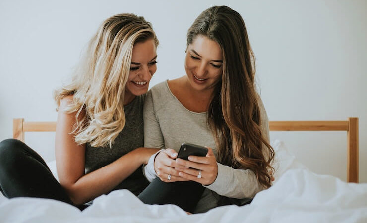 Two women looking at a phone looking at grabpoints while chilling on a bed