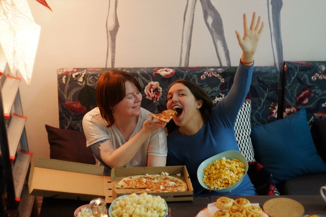 girls having fun watching TV and eating pizza