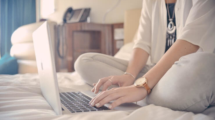 Woman wearing nice necklace sitting on her bed while using her laptop to search for movies to watch