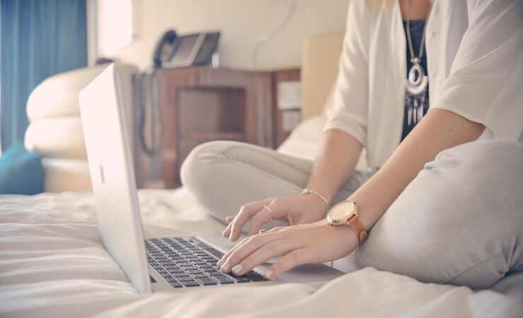 Woman wearing nice necklace sitting on her bed while using her laptop to search for movies to watch