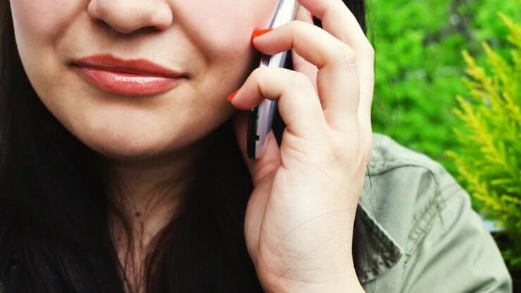 woman with black hair wearing green shirt talking on her cell phone with an orange manicure