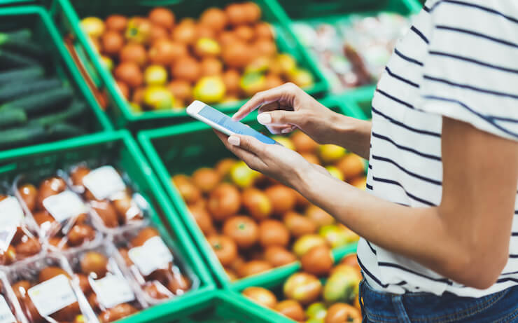 Woman using her cell phone to compare prices while grocery shopping at a store