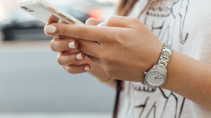 A woman with white manicure and wearing a silver watch using her iphone