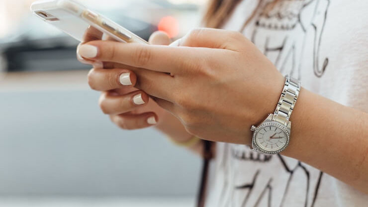 A woman with white manicure and wearing a silver watch using her iphone