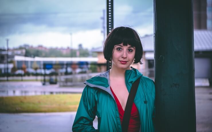 Young woman wearing a blue jacket leaning against a poll outside